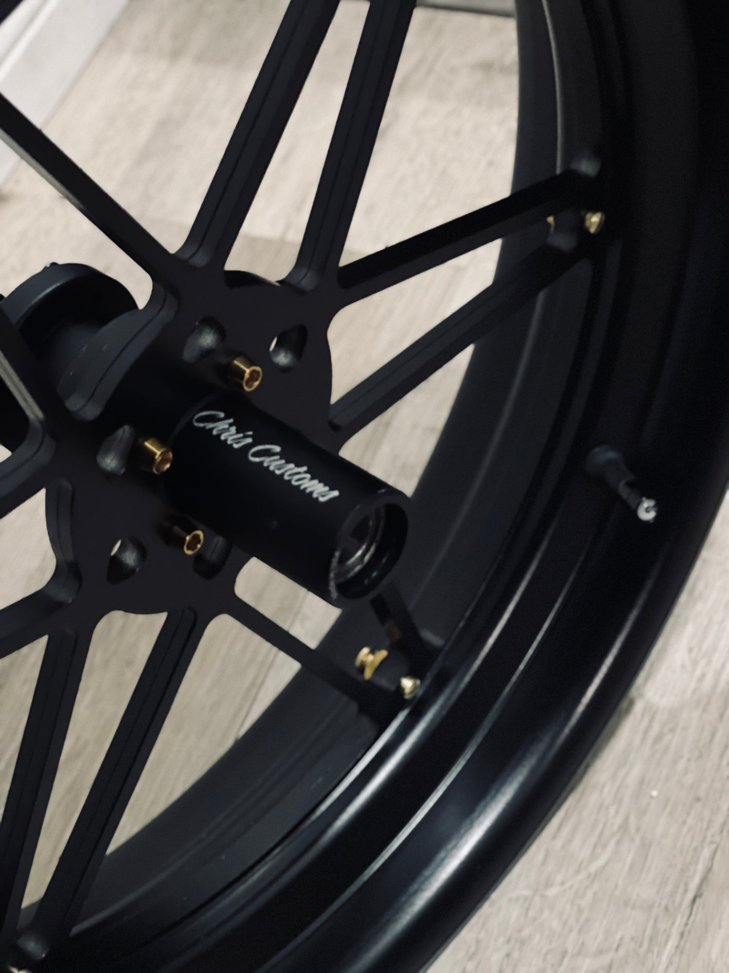 Close-up of a black motorcycle wheel with 'Chili Customs' branding on a light wooden floor.