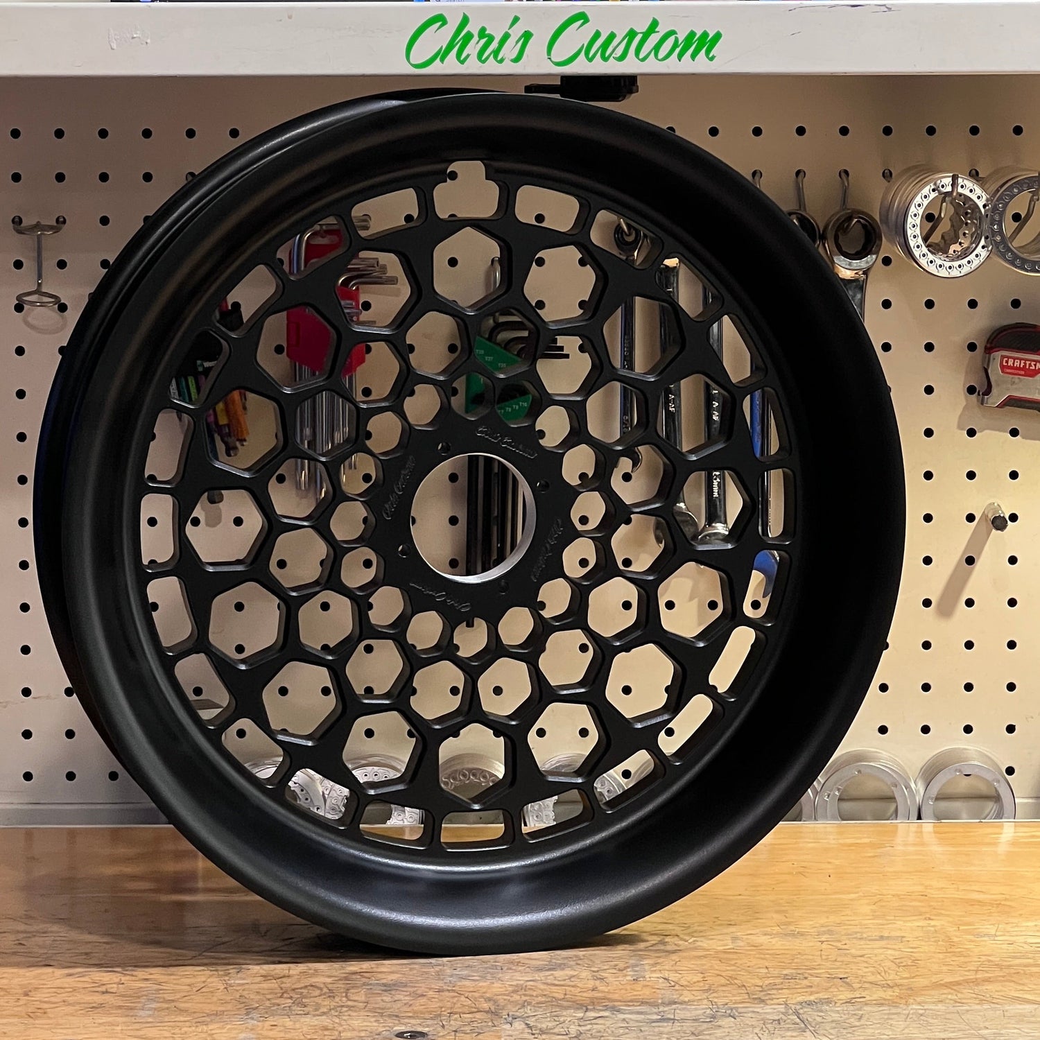Black decorative wheel on a wooden surface with 'Chris Customs' branding in the background.