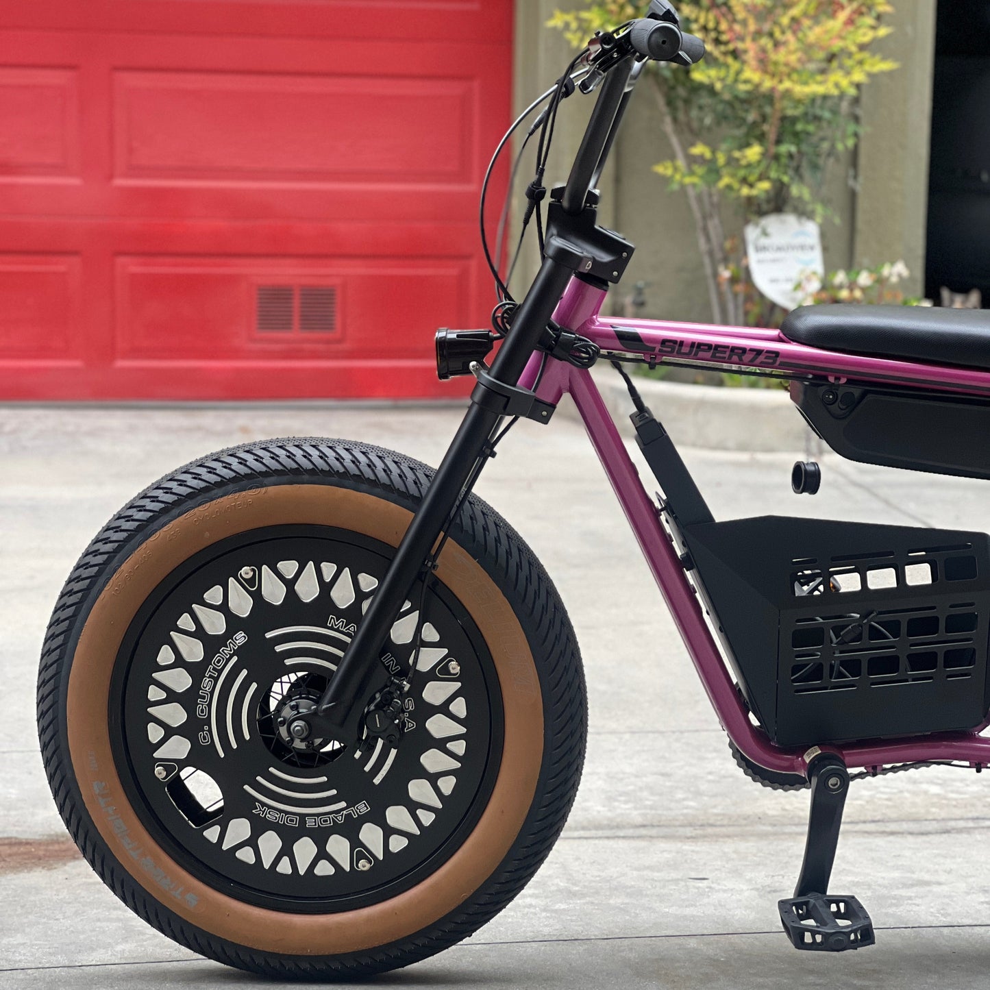 Purple electric bike with large wheels on a concrete surface, red garage door in the background