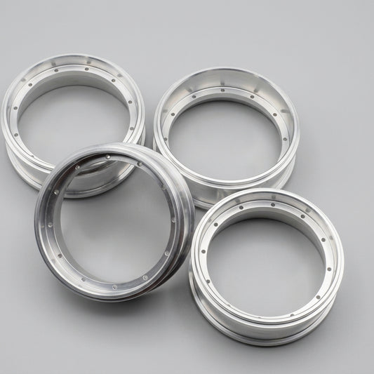 Four polished silver metal wheel rims arranged on a gray concrete floor.