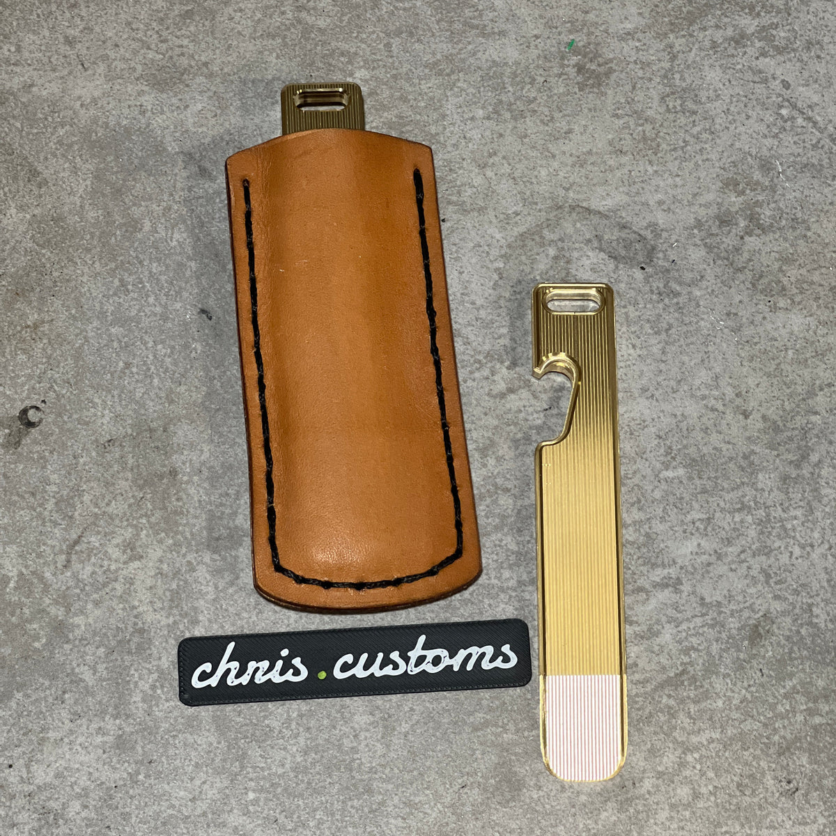 A tan leather key case with black contrast stitching and a brass key blade, displayed on a gray textured background with a 'chris.customs' brand tag.