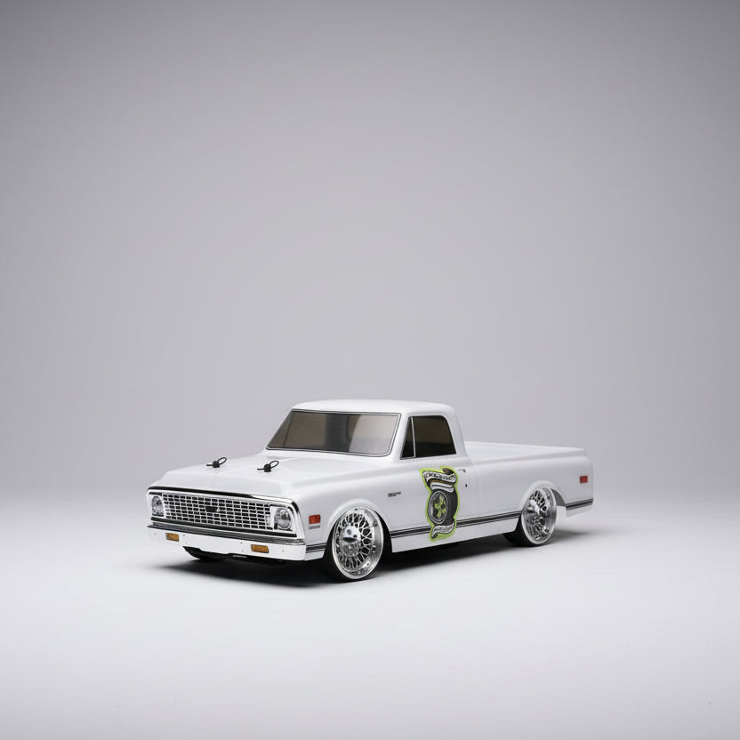 Model of a white truck with chrome details on a wooden surface, with tools and equipment in the background.