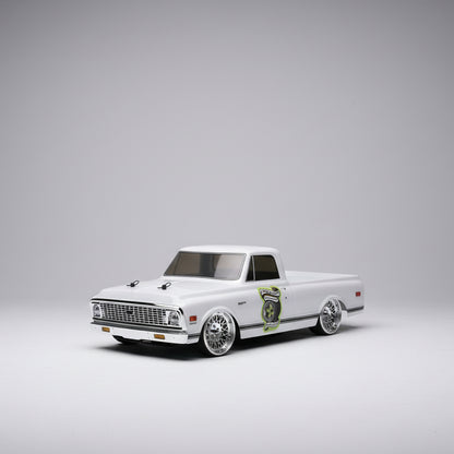 Model of a white truck with chrome details on a wooden surface, with tools and equipment in the background.