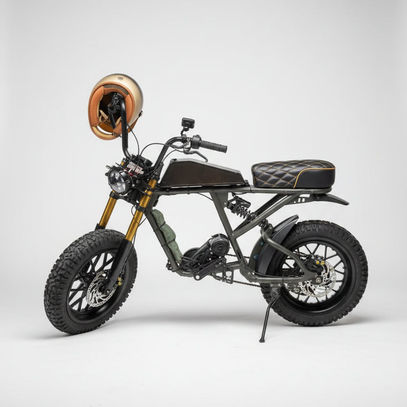 A custom-built electric fat tire bike with a matte black frame, black quilted seat, and a copper-colored round headlight, parked on a concrete patio in front of a red brick wall.