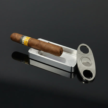 Cigar with a band on a metal tray next to a cutter on a dark surface with 'EAT DRINK NAP' text.