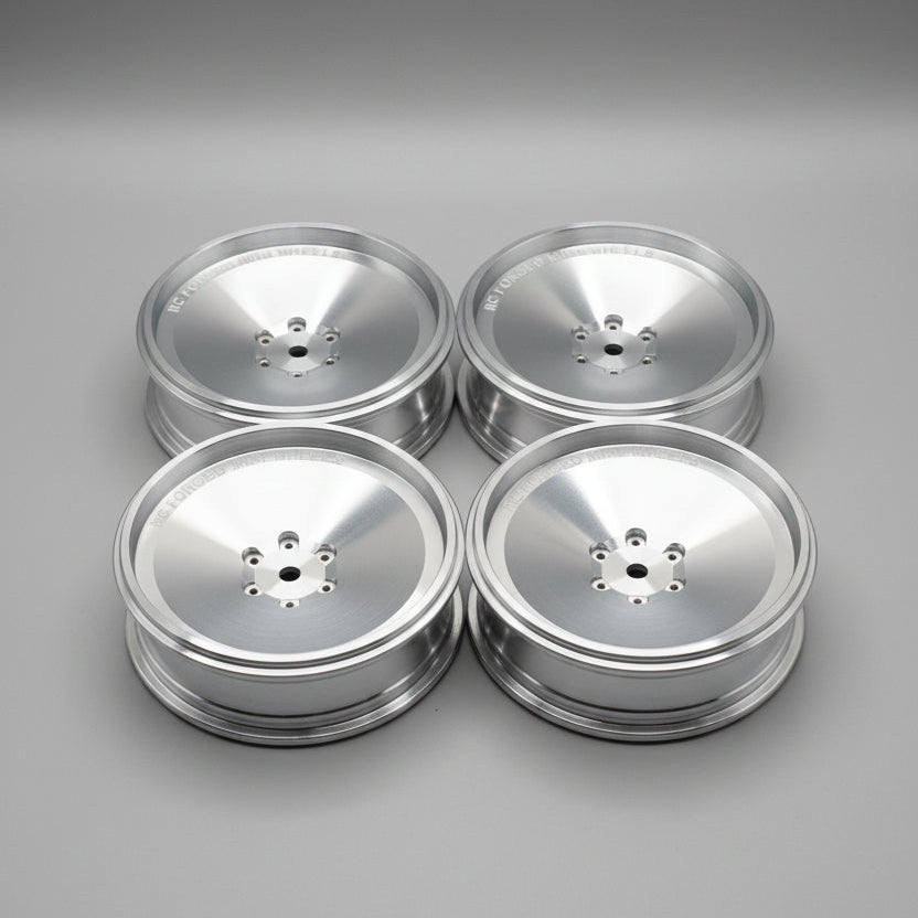 Four silver aluminum RC forged Mini Wheels displayed on a gray concrete floor.