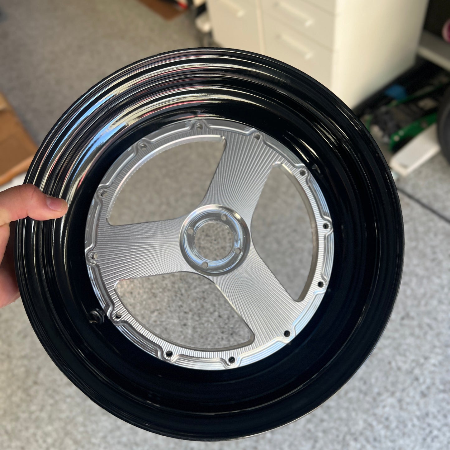 A close-up of a custom black and silver multi-spoke wheel rim held by a hand in a workshop setting.