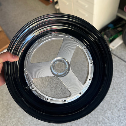 A close-up of a custom black and silver multi-spoke wheel rim held by a hand in a workshop setting.
