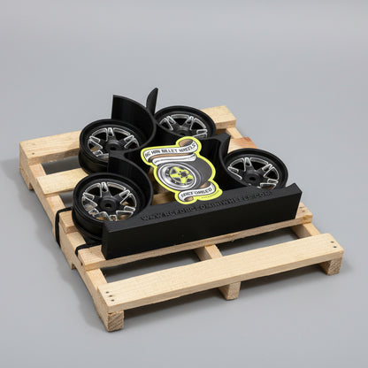 A set of four black anodized aluminum RC car wheels with bead-lock grip, designed for 1/10 scale models, displayed on a wooden surface.