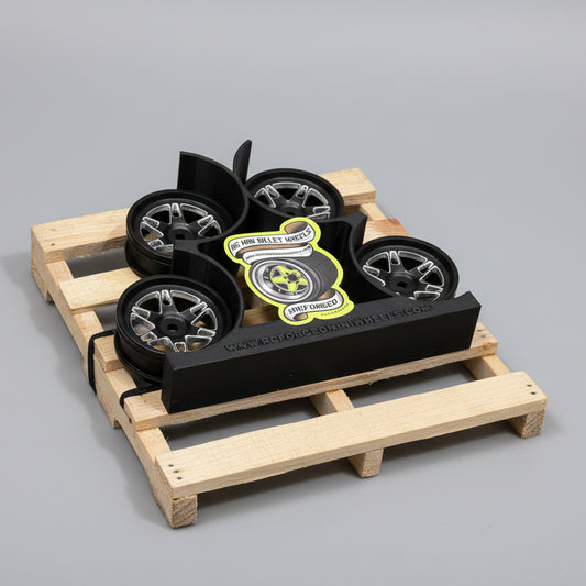 A set of four black anodized aluminum RC car wheels with bead-lock grip, designed for 1/10 scale models, displayed on a wooden surface.