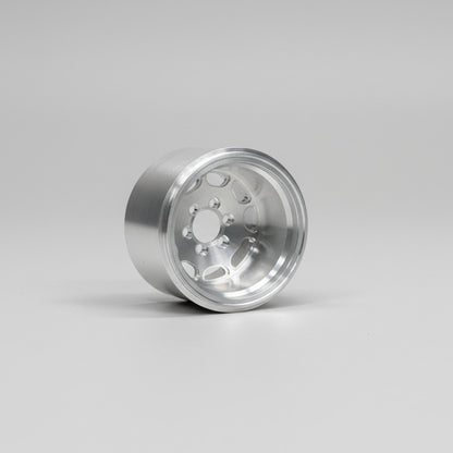 A hand wearing a green glove holding a silver aluminum RC car wheel with a solid pattern and no visible branding.