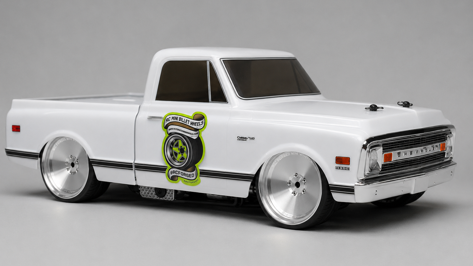 A white model pickup truck with chrome wheels, a custom lime green and black tire graphic on the side door, and a lowered stance, photographed on a seamless gray studio background.