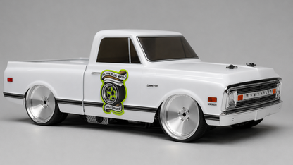 A white model pickup truck with chrome wheels, a custom lime green and black tire graphic on the side door, and a lowered stance, photographed on a seamless gray studio background.