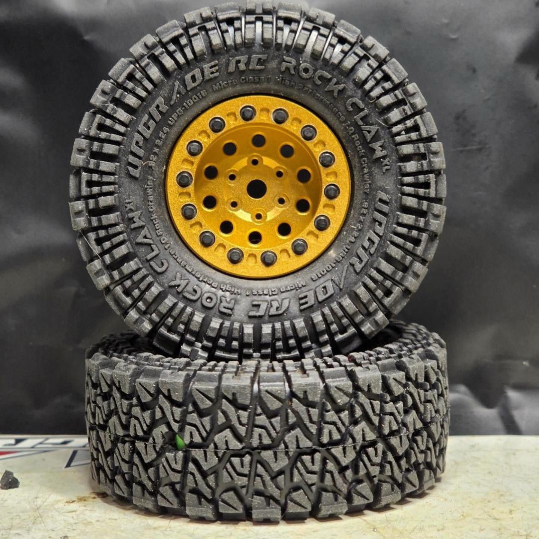 Two black off-road tires stacked on top of each other, mounted on bright yellow wheels, photographed against a dark gray backdrop.