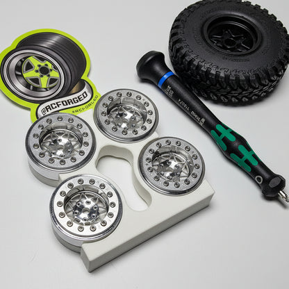 Set of metal wheel rims on a textured surface with a screwdriver and 'Forged' branding visible.