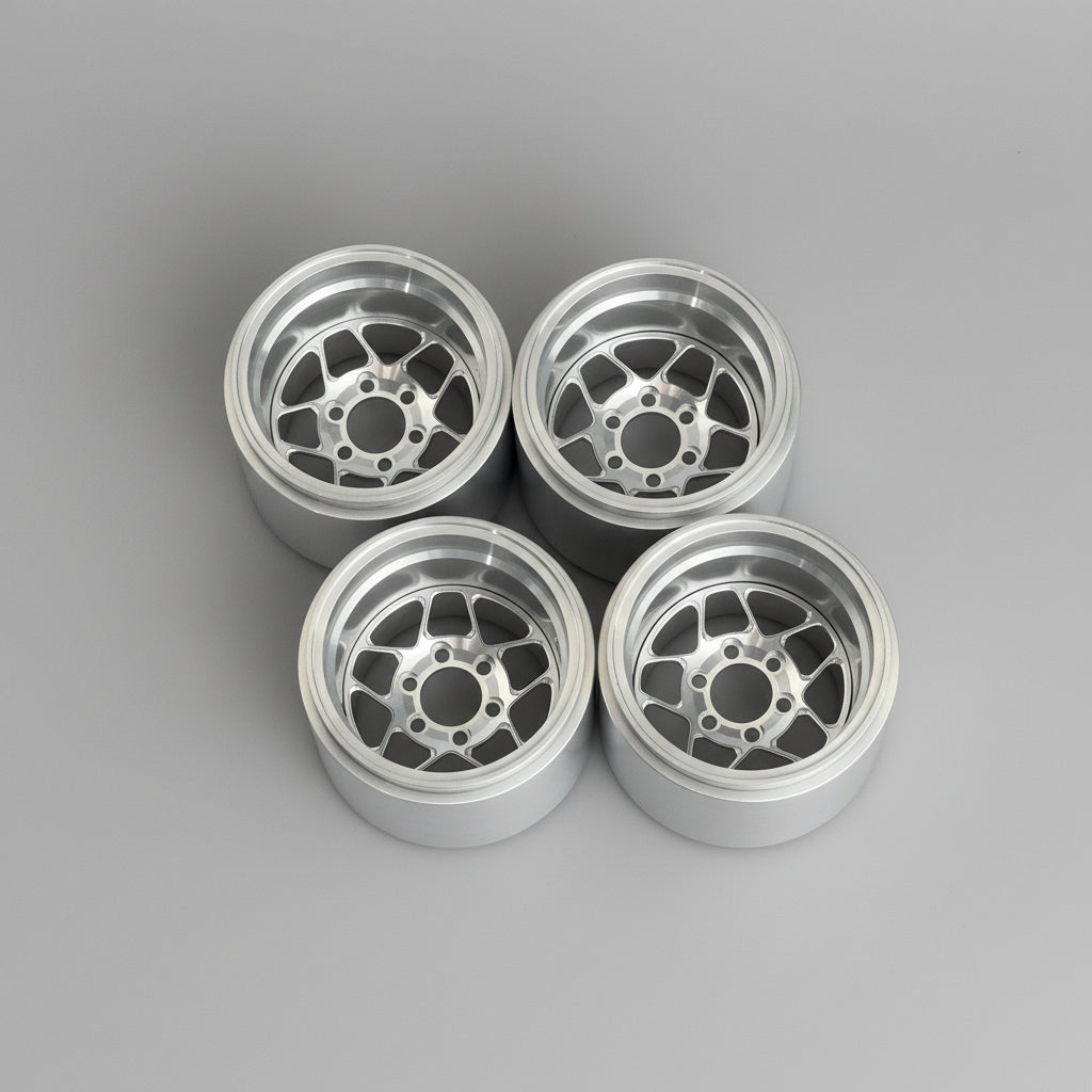 Four silver multi-spoke alloy wheels arranged in a 2x2 grid on a textured gray concrete floor.