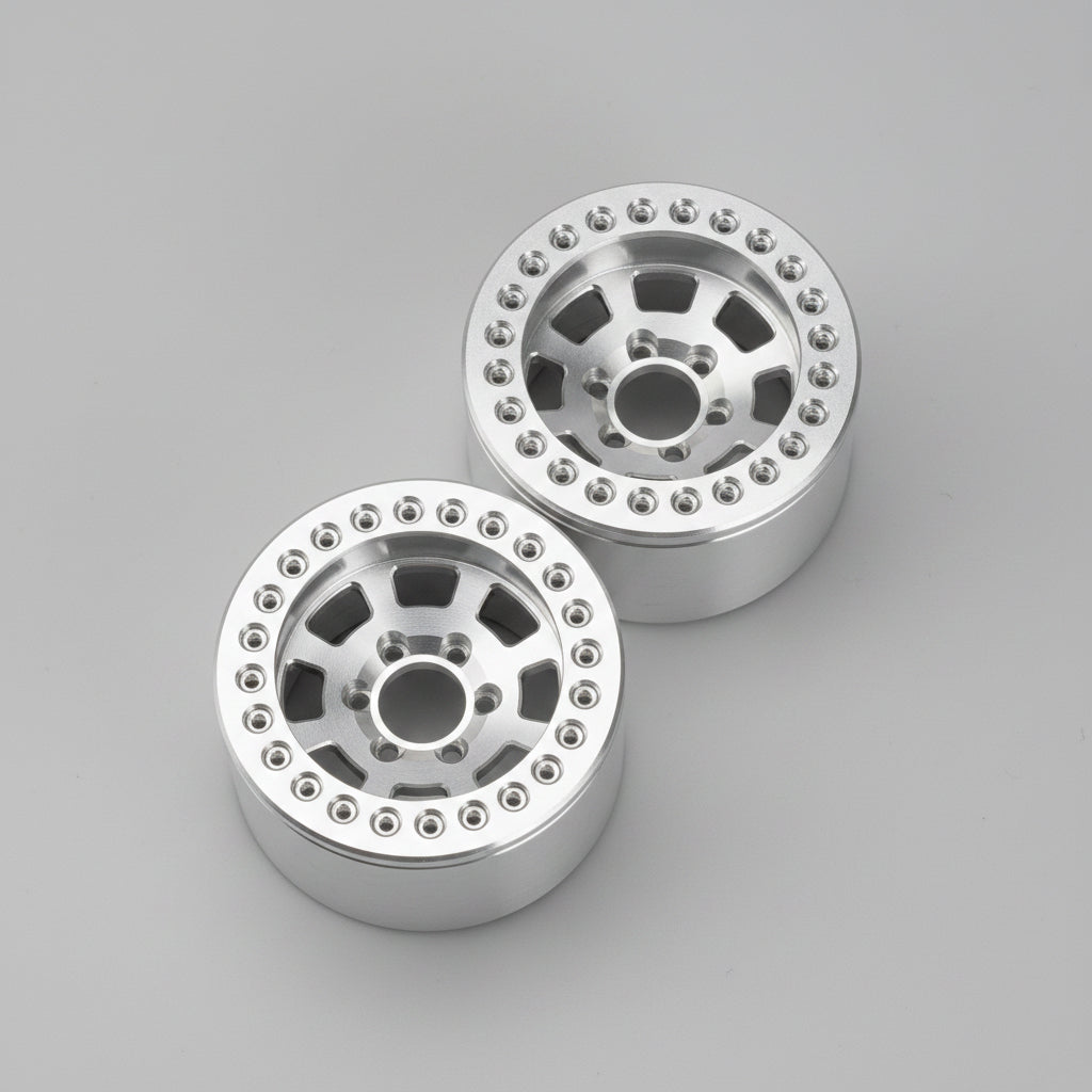 Two silver metallic off-road wheels with a multi-spoke design and bead edges, resting on a gray concrete floor.