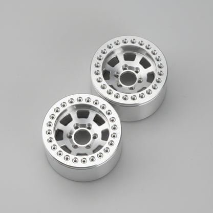 Two silver metallic off-road wheels with a multi-spoke design and bead edges, resting on a gray concrete floor.