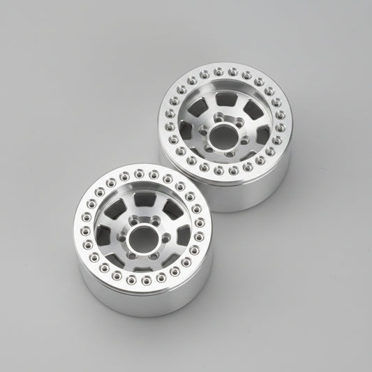 Two silver metallic off-road wheels with a multi-spoke design and bead edges, resting on a gray concrete floor.