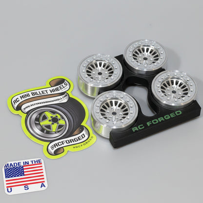 A set of four aluminum scale wheels for remote control vehicles, with bead locks and hardware, displayed on a wooden surface.