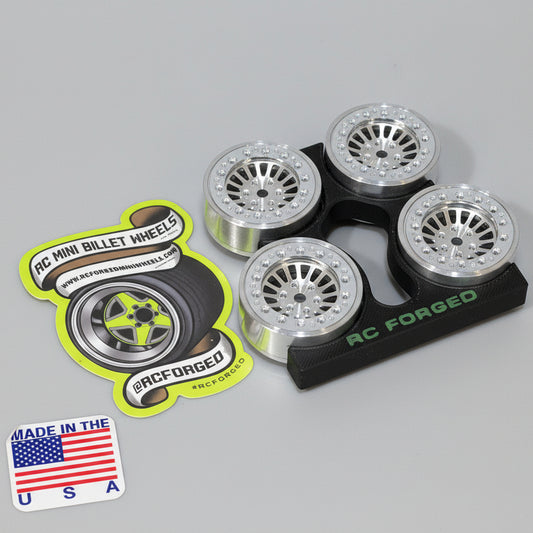 A set of four aluminum scale wheels for remote control vehicles, with bead locks and hardware, displayed on a wooden surface.