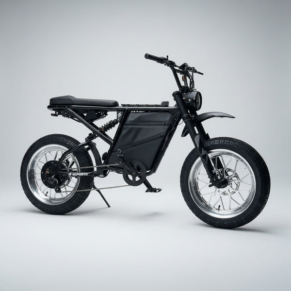 A black electric dirt bike with thick tires and silver spoked wheels, parked on a wet concrete street in front of a row of residential buildings with red garage doors.