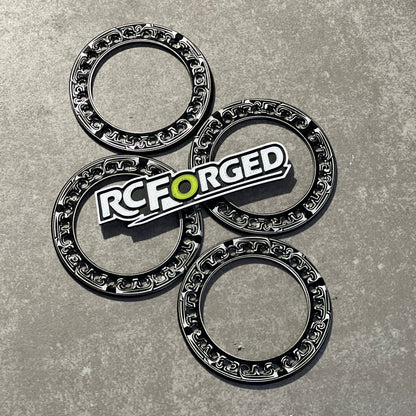 Four black and silver metallic ring-shaped components arranged on a gray textured surface, with a prominent RC FORGED logo badge placed over the center piece.