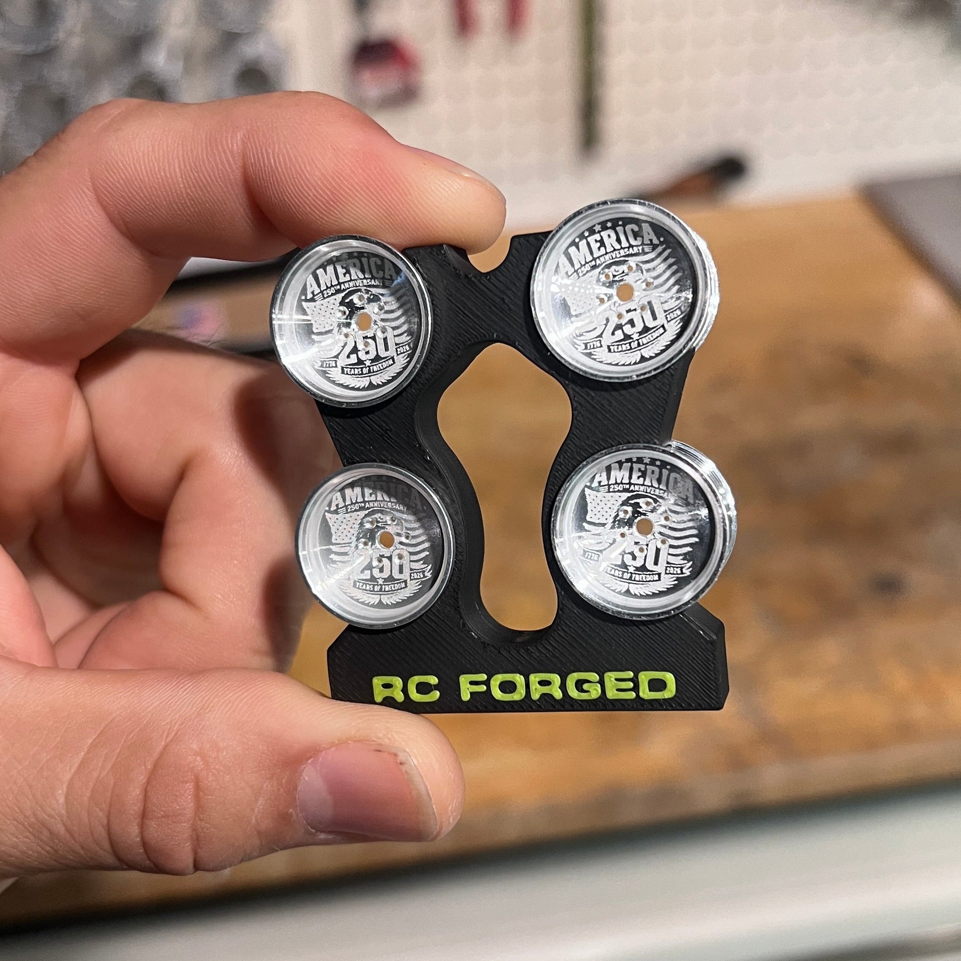 Hand holding a set of RCFORGED car wheels with a blurred workshop background