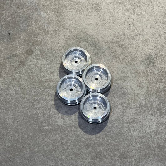 Four silver metallic circular components with a ribbed center design, arranged in a 2x2 grid on a textured gray concrete surface.