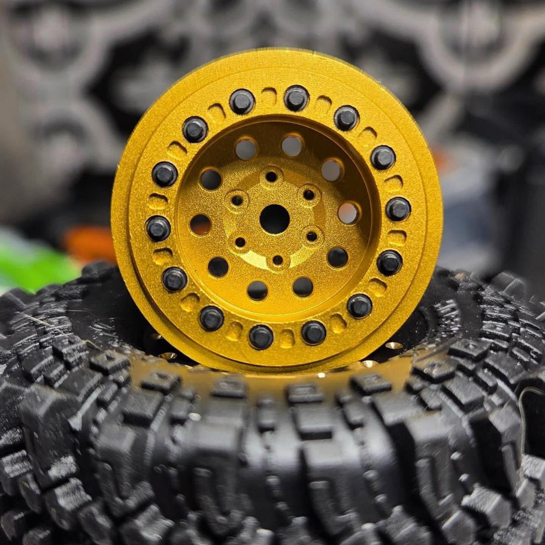A close-up of a bright yellow RC crawler wheel rim with black spoke accents, resting on top of a black knobby tire.