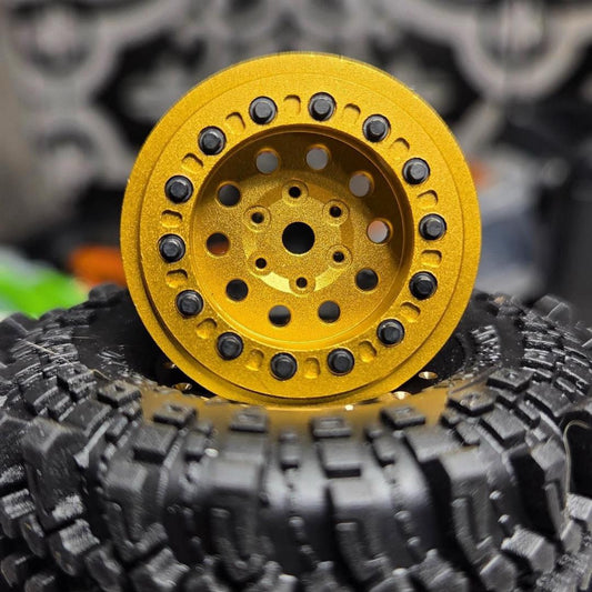 A close-up of a bright yellow RC crawler wheel rim with black spoke accents, resting on top of a black knobby tire.